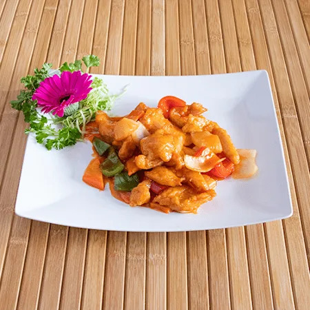Thai stir fry with chicken and vegetables on a white plate, garnished with a pink flower and herbs