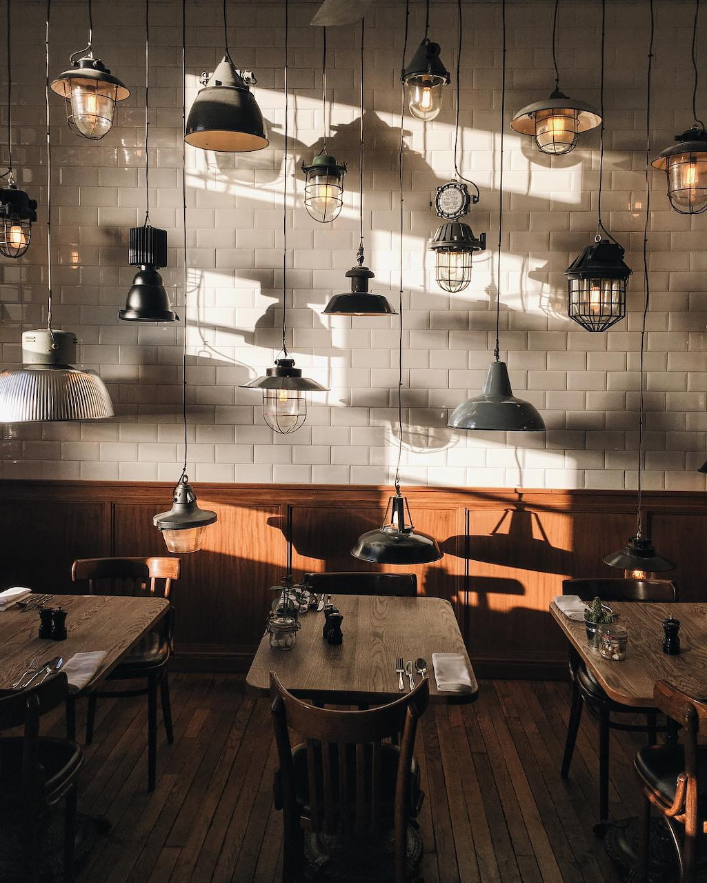 Cozy cafe interior with wooden tables and multiple hanging pendant lights on a tiled wall