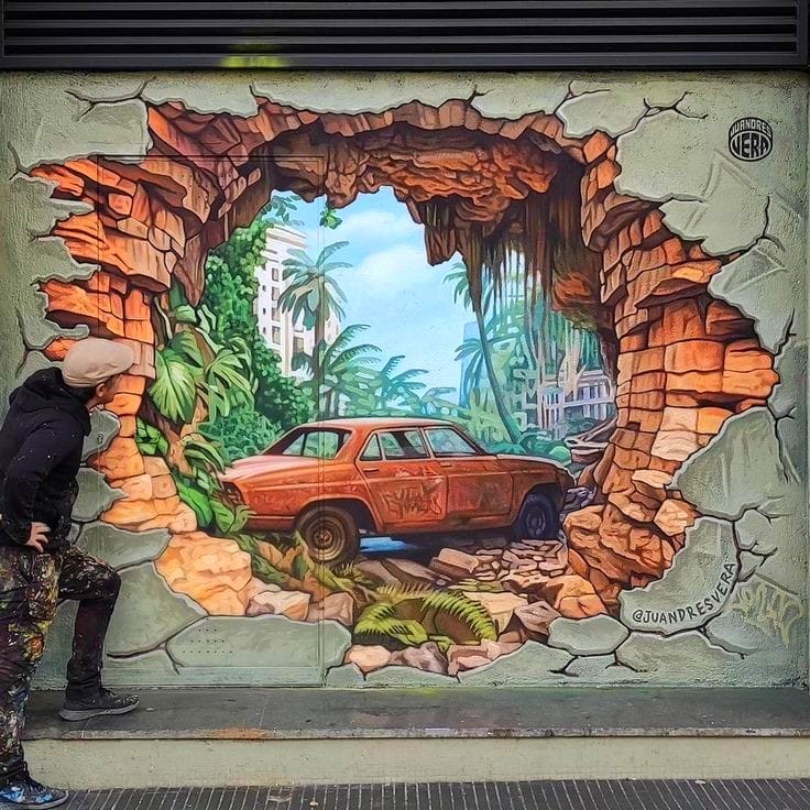 Trompe-l'oeil street art showing vintage car bursting through painted cracked wall into tropical landscape