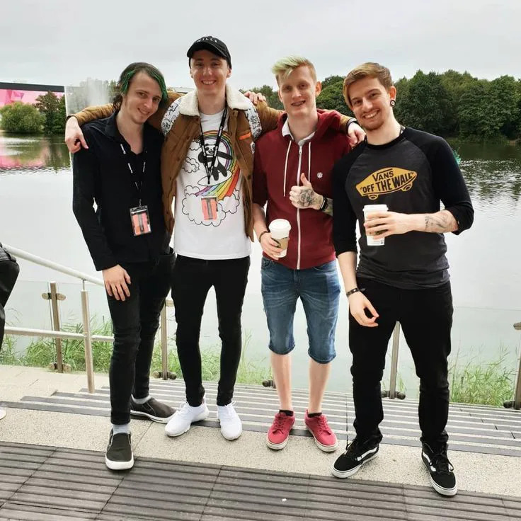 Four young men posing on a deck by a lake with drinks in hand