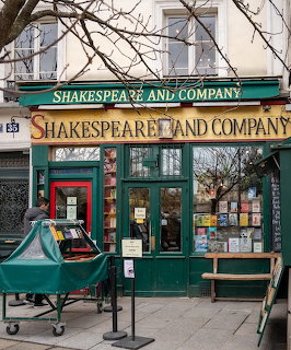 Green facade of Shakespeare and Company bookstore in Paris with display windows and bare tree branches
