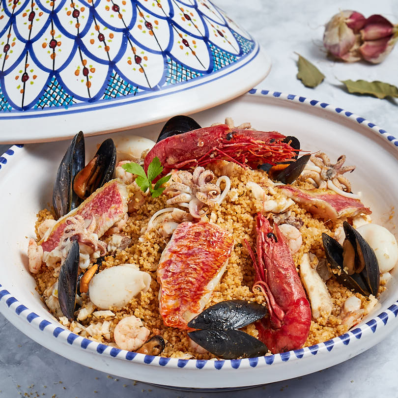 Bowl of Sicilian seafood couscous with prawns, mussels, calamari, and octopus on a white plate