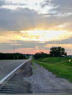 Rural highway stretching toward a small town at sunrise with dramatic clouds and sun rays