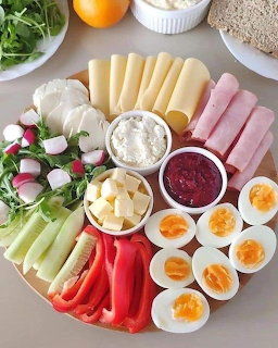 Round wooden board with boiled eggs, ham, cheese, vegetables, radishes, and dips arranged neatly