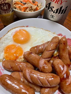 Sunny-side up eggs and grilled sausages on a white plate with beer and side dishes