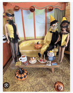 Three fashion dolls in Halloween costumes in a decorated room with pumpkins and treats