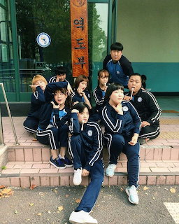 Group of Korean students in navy blue school uniforms posing together outside a school entrance