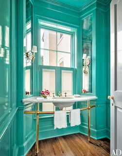 Elegant teal bathroom with marble console sink, brass fixtures, wall sconces, and large window