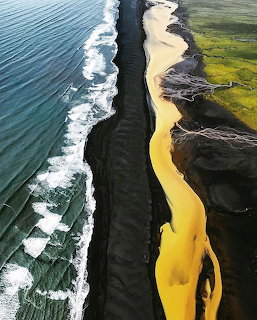 Aerial view of black sand beach with turquoise waves and yellow river cutting through green mossy landscape in Iceland