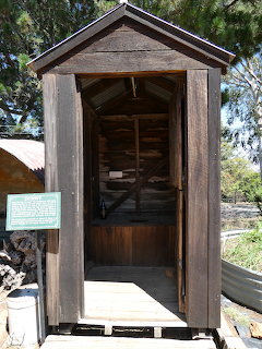 Old wooden outhouse with weathered siding and open door revealing wooden bench seat inside