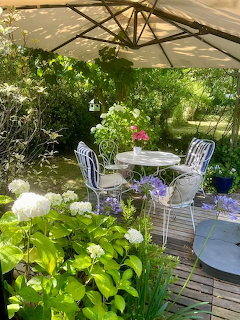 White patio table and chairs under a garden umbrella surrounded by flowers and green plants