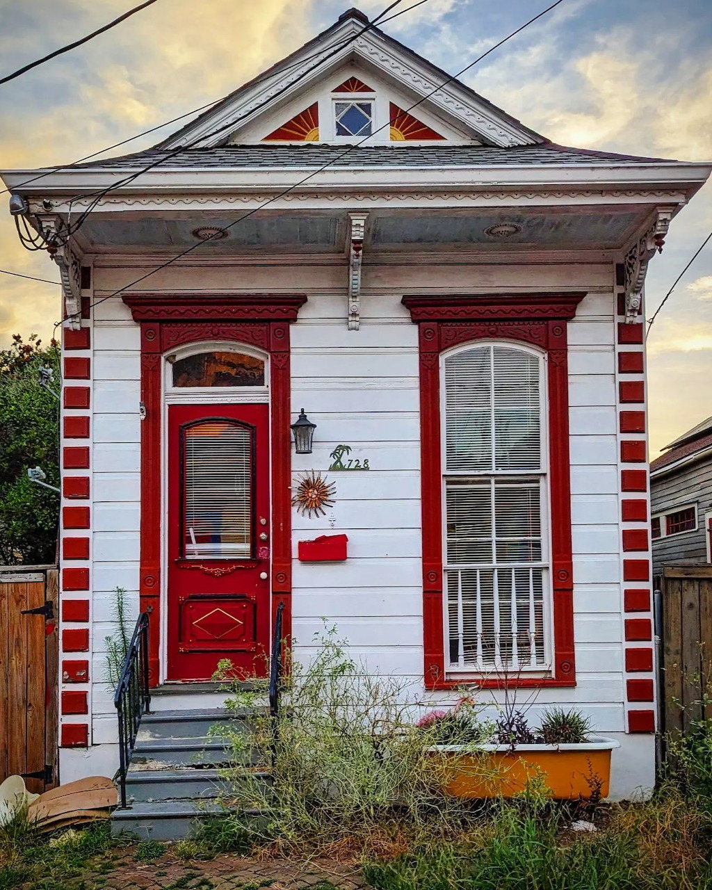 Small white cottage with red striped trim and red door under dramatic sunset sky