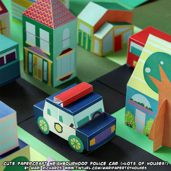 Papercraft police car beside colorful paper houses in a miniature neighborhood
