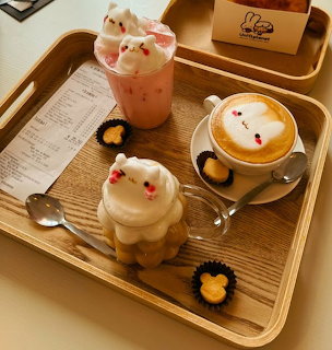 Three cute decorated coffee drinks on wooden trays with spoons, cookies, and a receipt