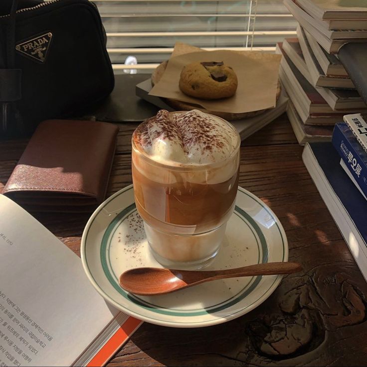 Glass of whipped coffee on a saucer with books, a spoon, and a cookie on a wooden table