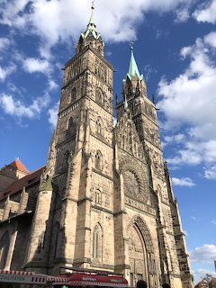 Tall Gothic stone church with twin towers and spires against blue sky with white clouds