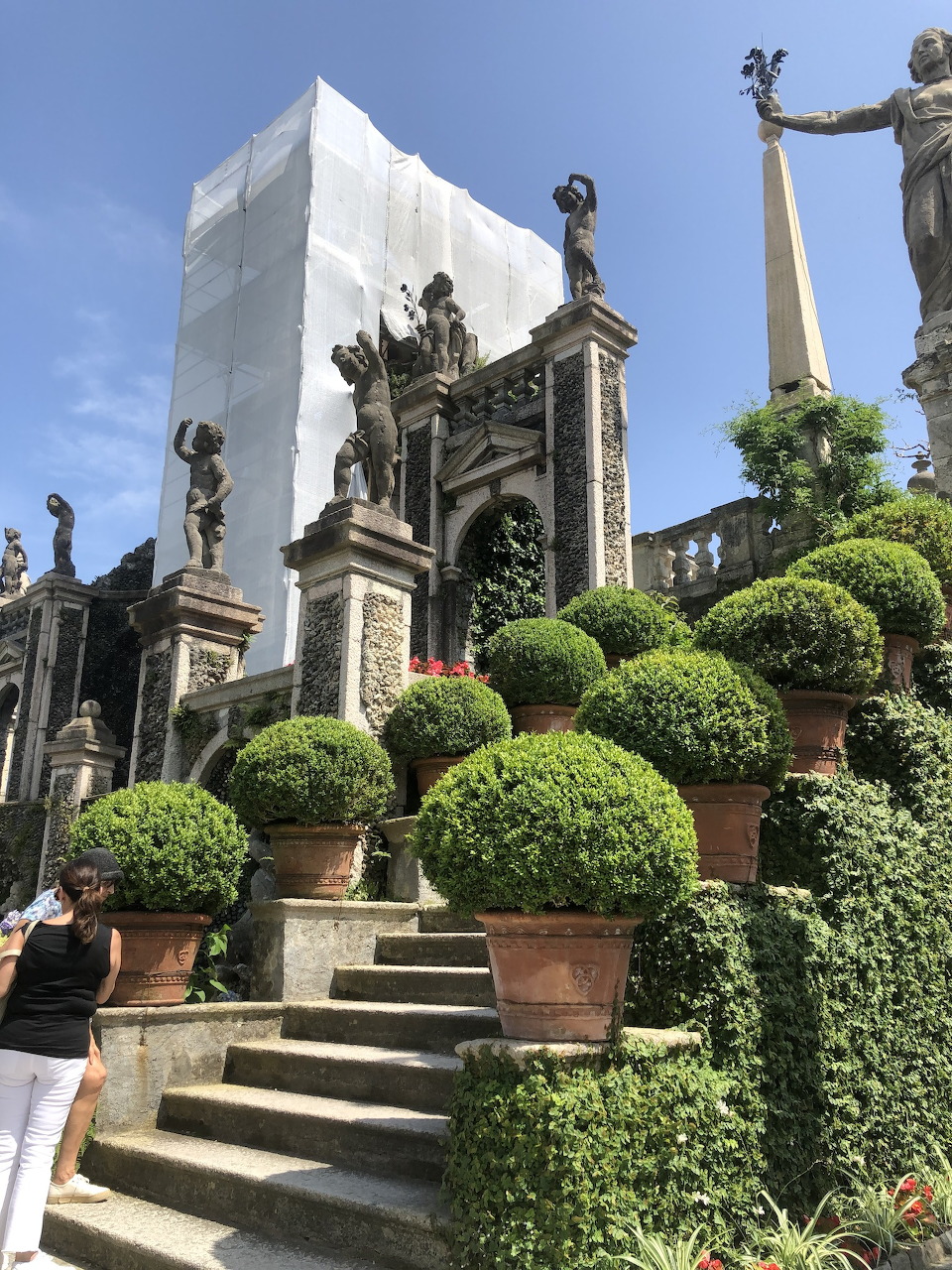 Baroque garden with clipped topiary spheres, stone statues, steps, and a scaffolded building at Stresa
