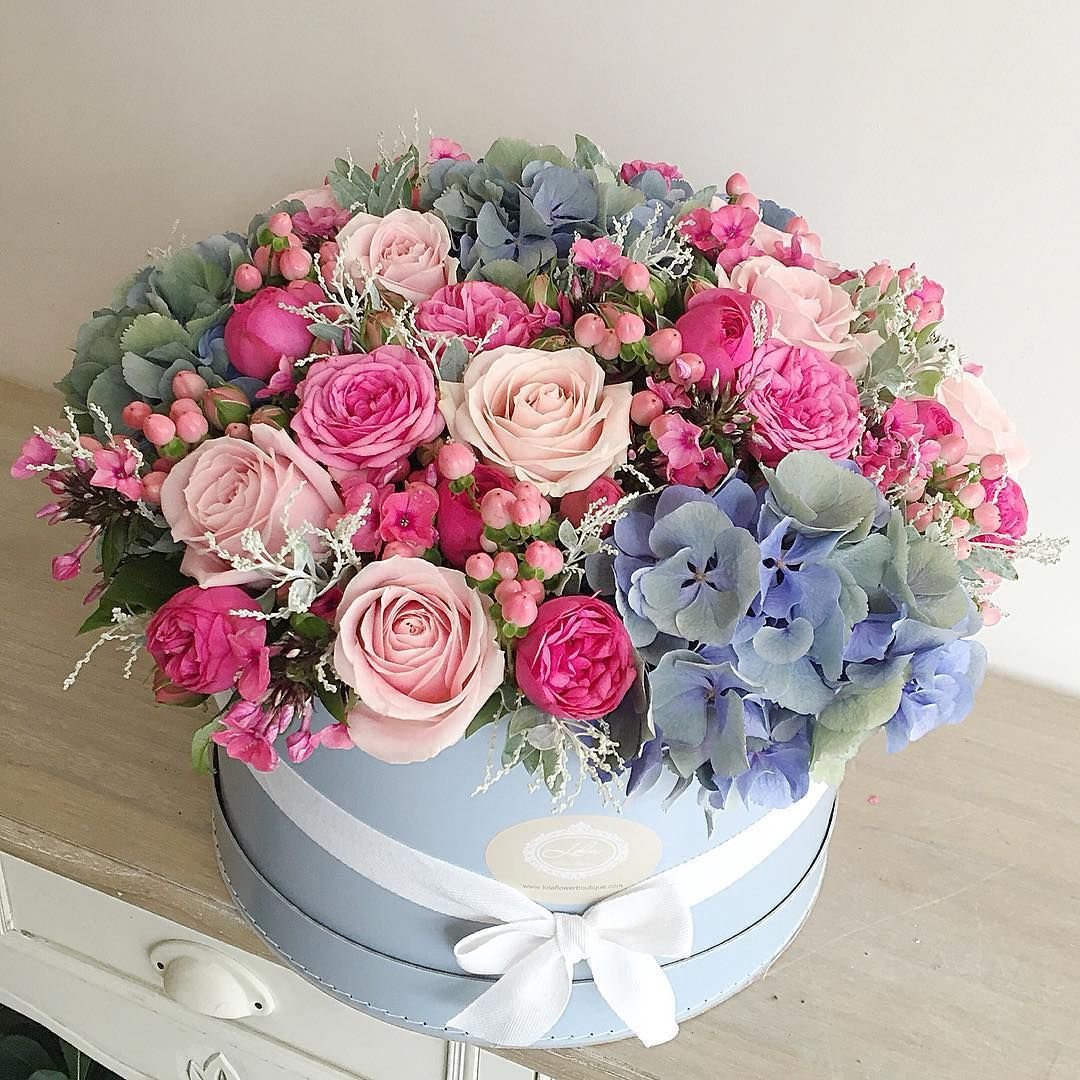 Luxurious flower bouquet with pink roses, blue hydrangeas, and mixed blooms in white gift box with silver ribbon