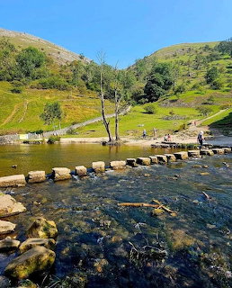 Stepping stones across a river in a green valley with hills under blue sky