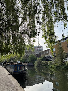 Narrowboats moored on a quiet London canal lined with willow trees and brick buildings