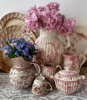 Red and brown transferware pitchers and vases with pink and blue flowers on lace doily