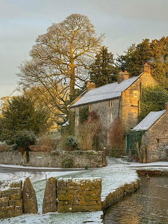 Stone cottage with snowy garden and bare winter trees in golden sunset light