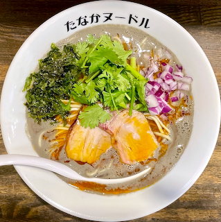 Bowl of ramen with eggs, pork, seaweed, cilantro, and vegetables in broth on wooden table