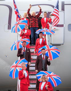 Man in plaid shirt with airline crew on plane stairs holding British and American flags