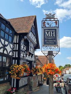 Traditional Tudor building with timber framing, hanging pub sign, and orange flower baskets under blue sky