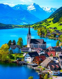 Alpine village with church on turquoise lake surrounded by mountains