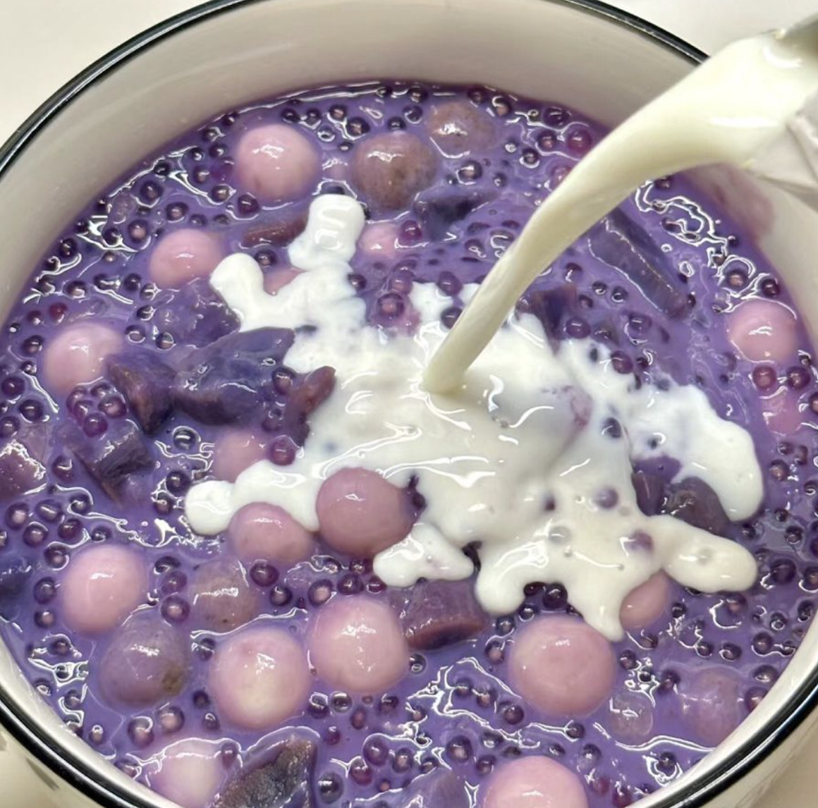 Purple ube sago dessert with tapioca pearls and coconut milk in white bowl