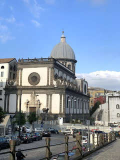 Historic domed church facade beside a street in Naples under a blue sky