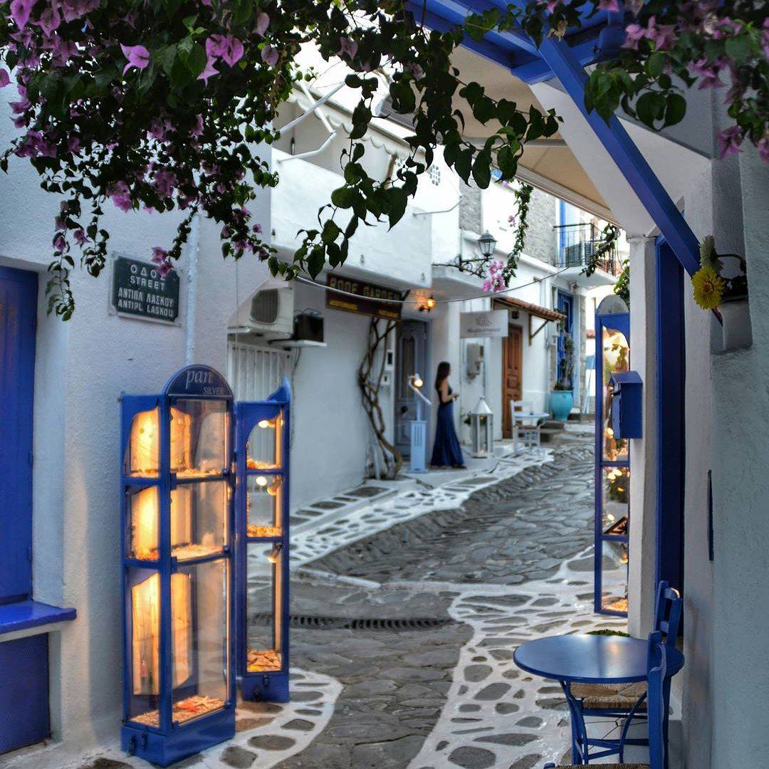 Whitewashed alley with blue windows and purple flowers in Greek island town at twilight