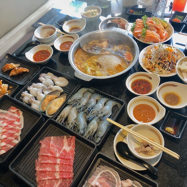 Table with a bubbling hot pot, seafood, sliced meat, dumplings, and dipping sauces