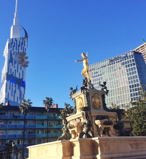 Golden statue atop ornate fountain monument in Batumi town square with modern buildings