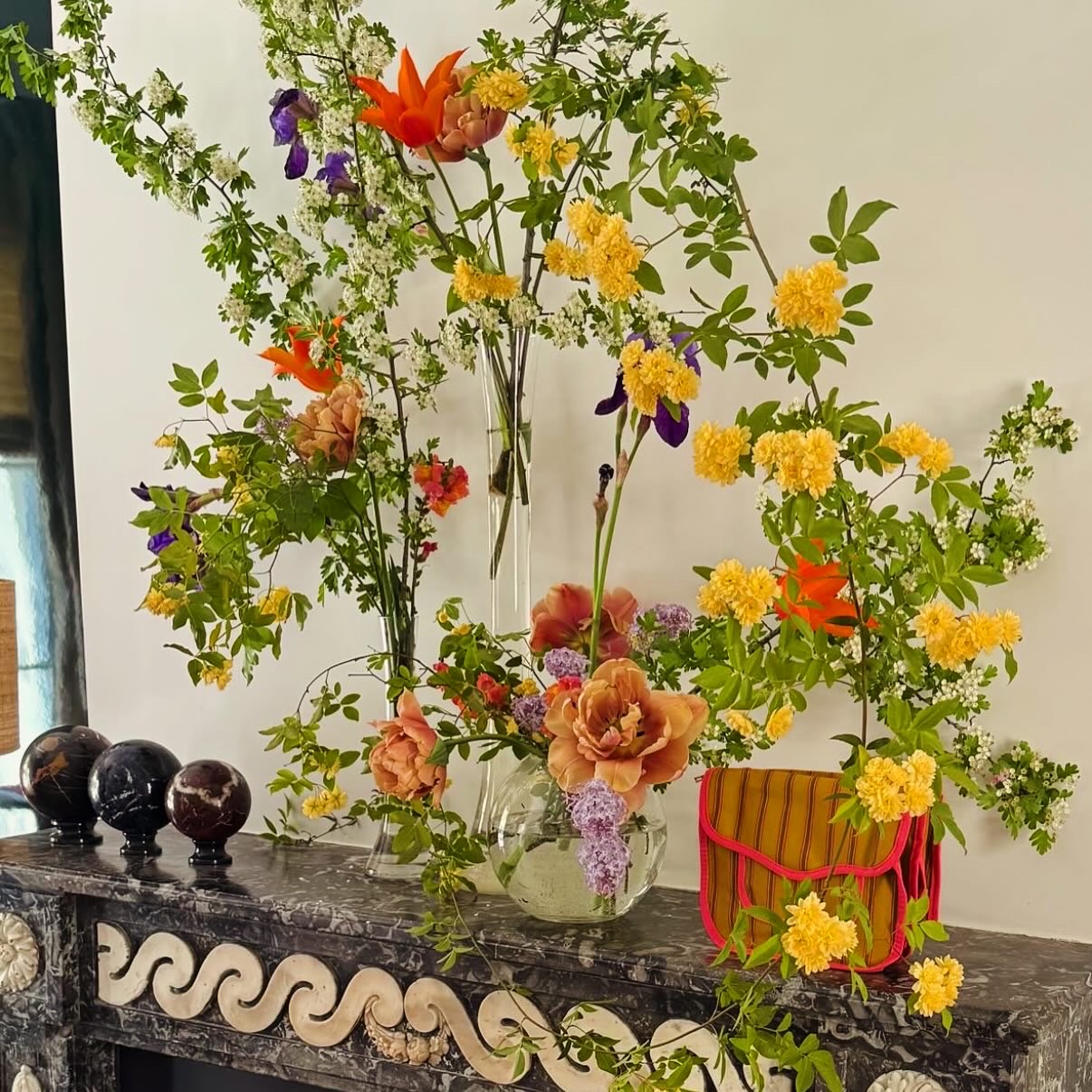 Vibrant spring flower arrangement with mixed colorful blooms displayed on dark wooden shelf with carved snake decoration
