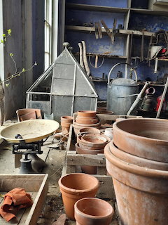 Rustic potting table with terracotta pots, scale, watering can, and garden tools