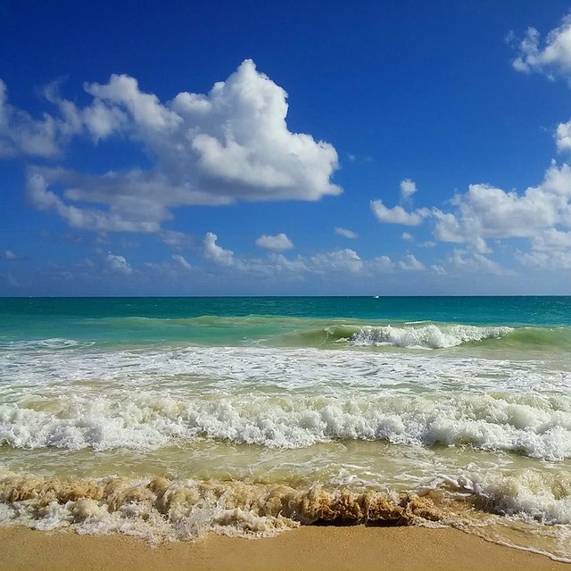 Waves breaking on a sandy beach beneath a blue sky with white clouds