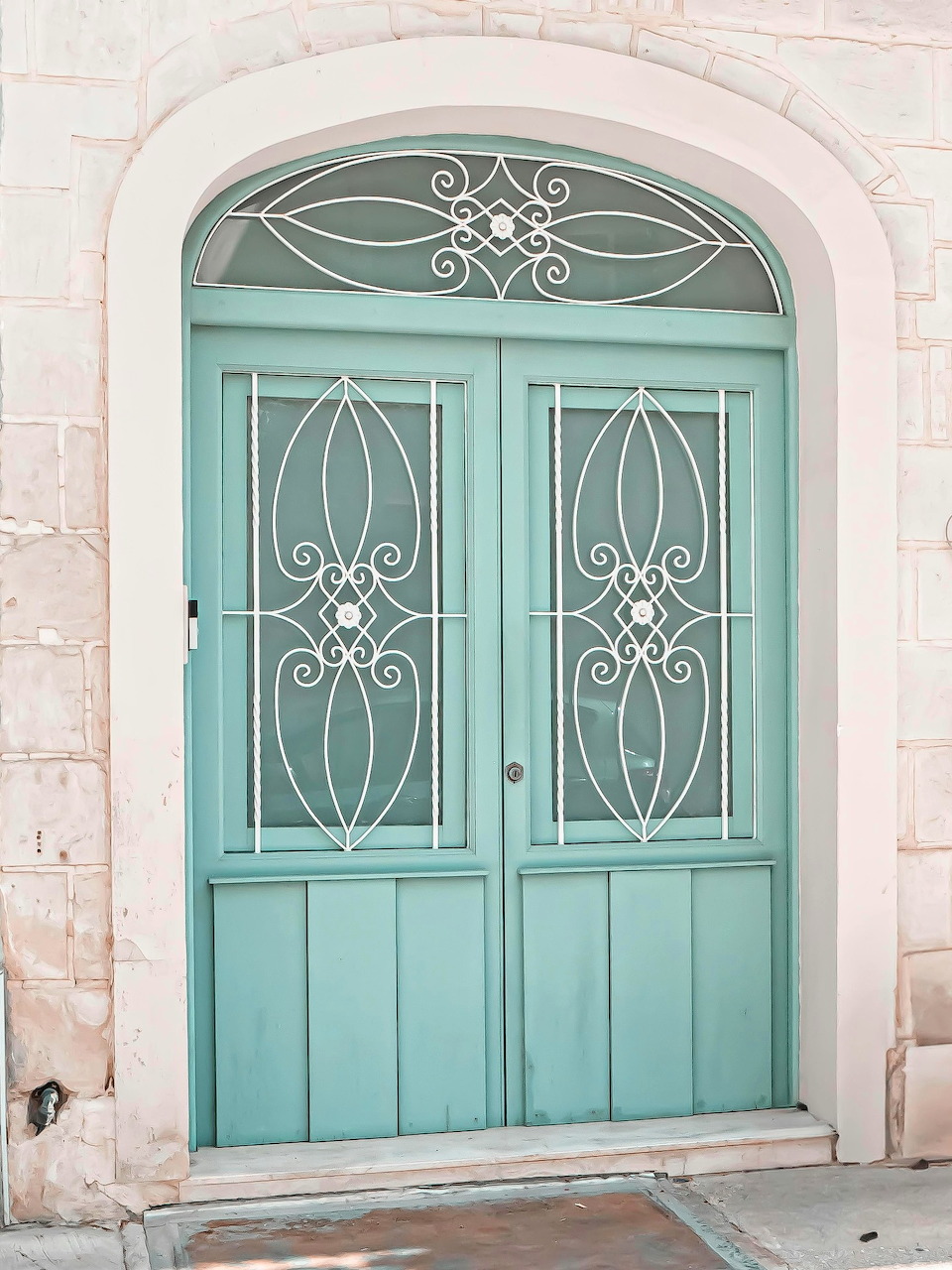 Turquoise arched double door with ornate wrought iron details in a stone doorway