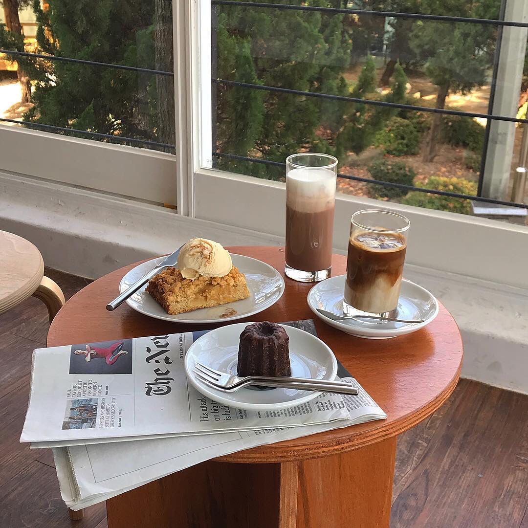 Coffee drinks and pastries on round table by window with natural light
