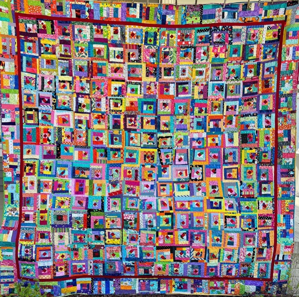 Colorful patchwork quilt with hundreds of small fabric squares in rainbow colors arranged in geometric log cabin pattern