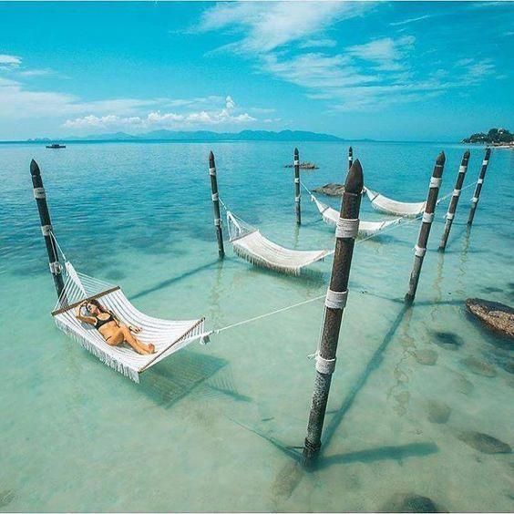 Woman resting in a hammock over shallow turquoise water at a tropical beach