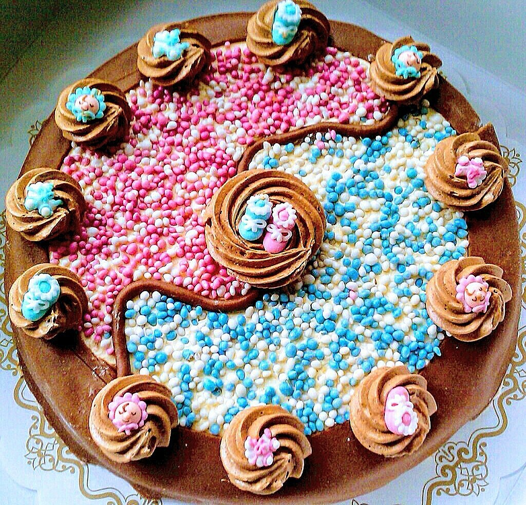 Baby shower cake with pink and blue sprinkles, gold decorations, and miniature fondant baby shoes on top