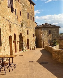 Sunlit medieval stone buildings with arched doorways around a piazza in San Gimignano, Italy