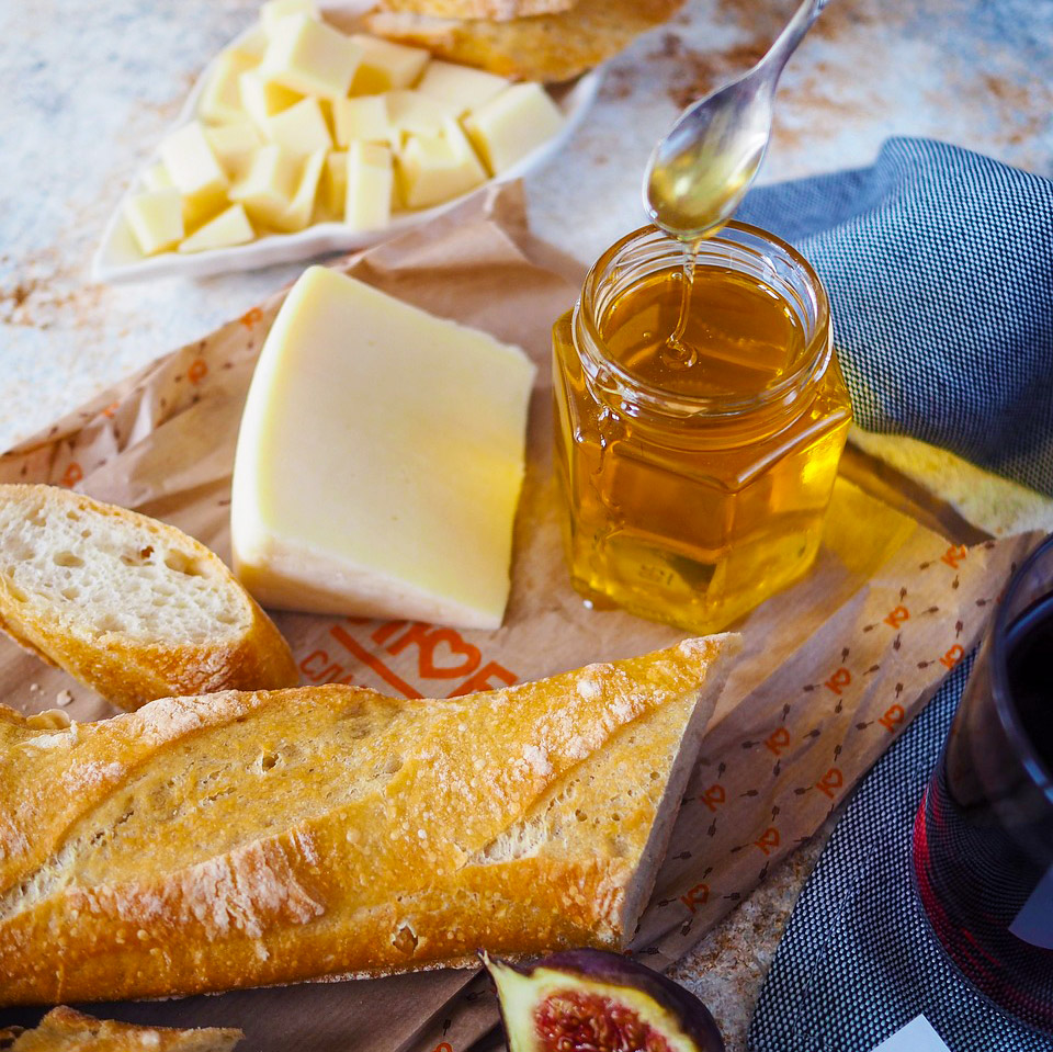 Rustic wooden board with bread, cheese, and honey jar