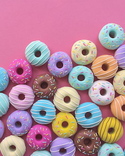 Assorted colorful glazed donuts with sprinkles on pink and purple background