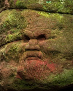 Carved human face in a mossy rock wall