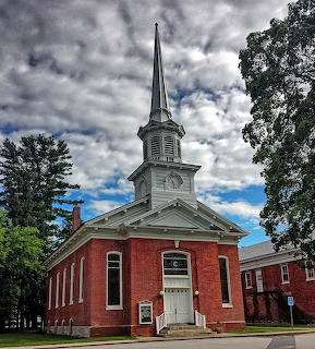 Red brick church with tall white steeple and clock tower under cloudy sky in Swanton Vermont