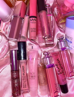 Collection of pink lip gloss tubes and products arranged on pink satin fabric