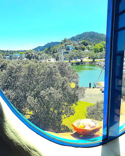 Rounded blue window frame at Hundertwasser Museum overlooking Whangarei harbour with green hills and trees